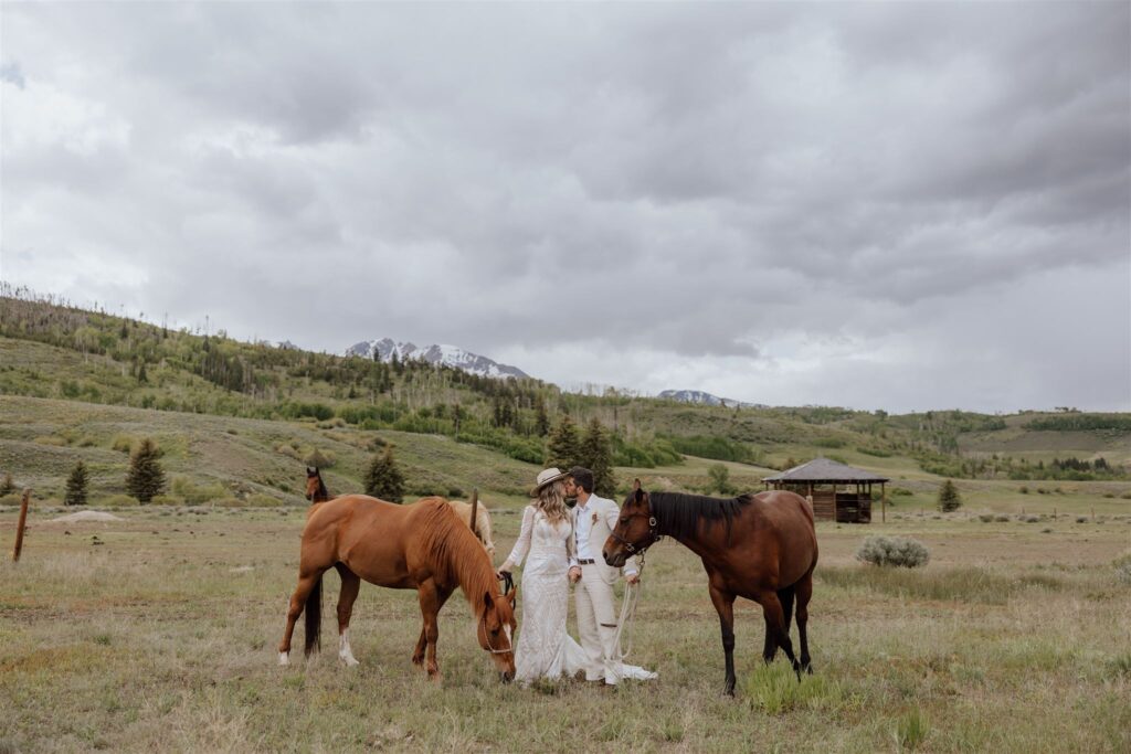 bride and groom with horses in a meadow with mountains in the background