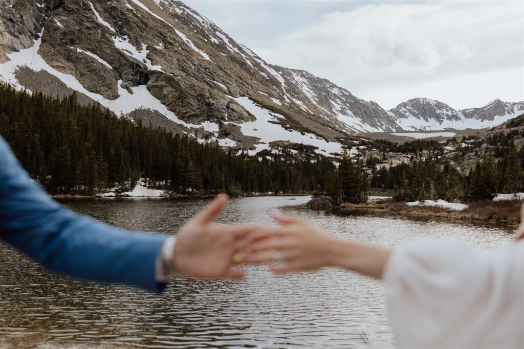 bride and groom hands reaching to each other out of focus with mountains in background