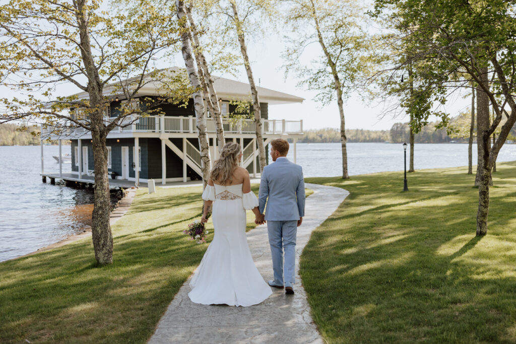 Bride and groom walking together down a path with birch trees and a boathouse in the background