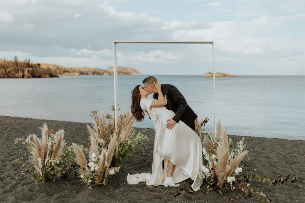 bride and groom kissing on black beach in Minnesota after ceremony.