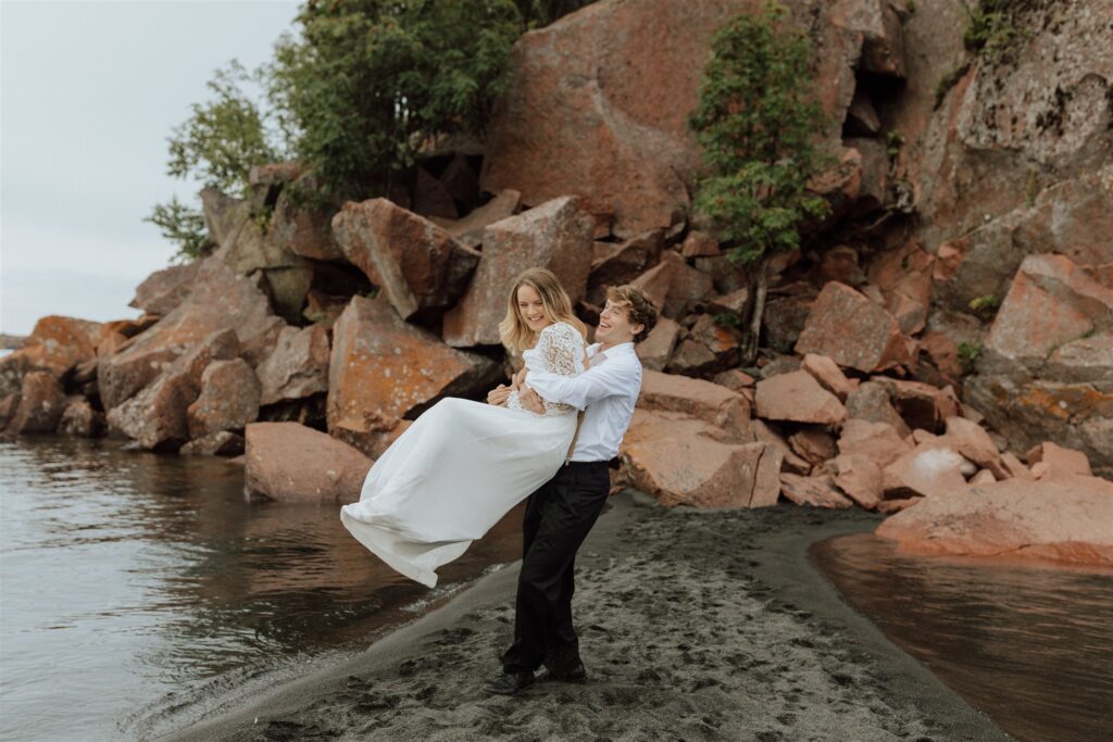 groom spinning bride on a black sand beach in Minnesota with red rocks in the background.