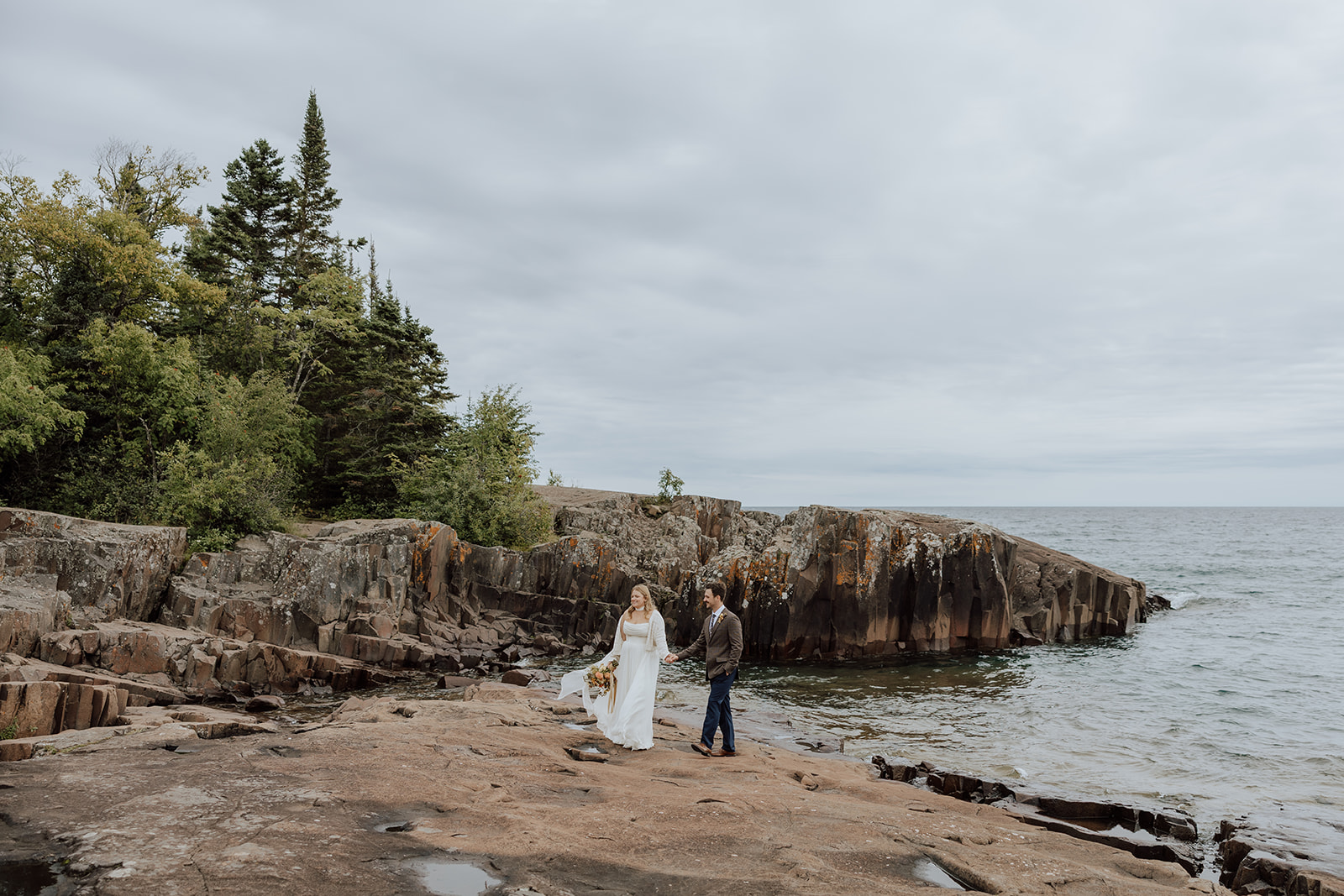 bride and groom in minnesota walking along a rocky shorline