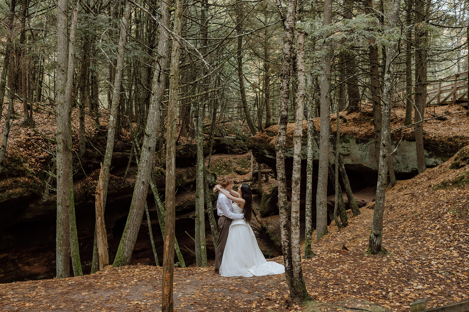 couple in wedding attire embracing in a forest with a rocky gorge behind them
