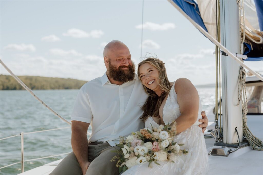 bride and groom smiling together sitting on a sailboat