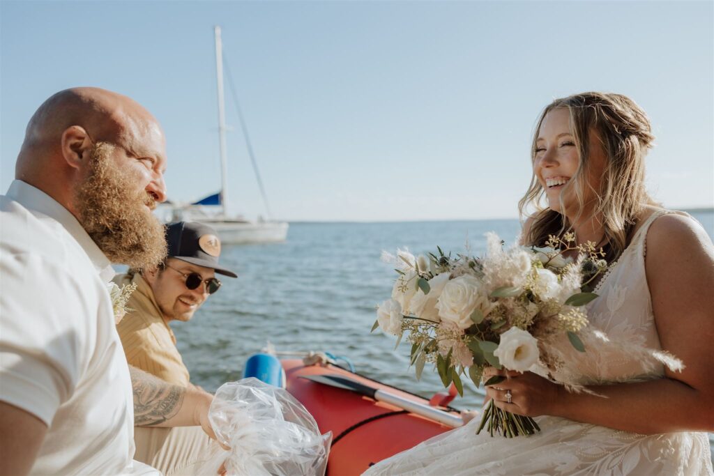 bride and groom on a raft boat with a sailboat in the background